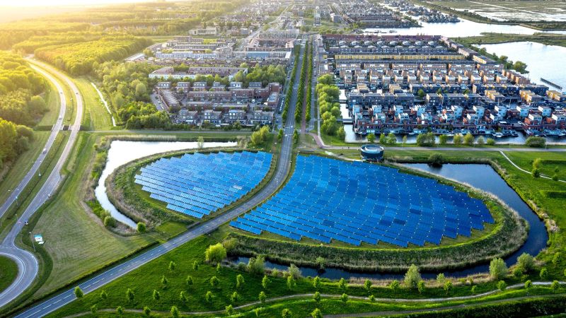 Luftaufnahme eines modernen, nachhaltigen Viertels in Almere, Niederlande. Eine große , runde Ansammlung von Solaranlagen ist im Zentrum zu sehen.