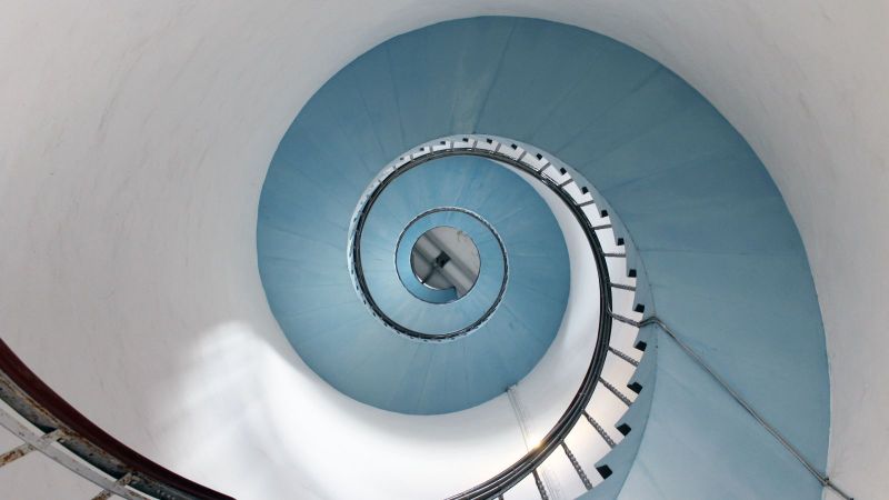 Blick von unten an einer spiralförmig verlaufenden Treppe entlang, die hoch in einen Turm führt.