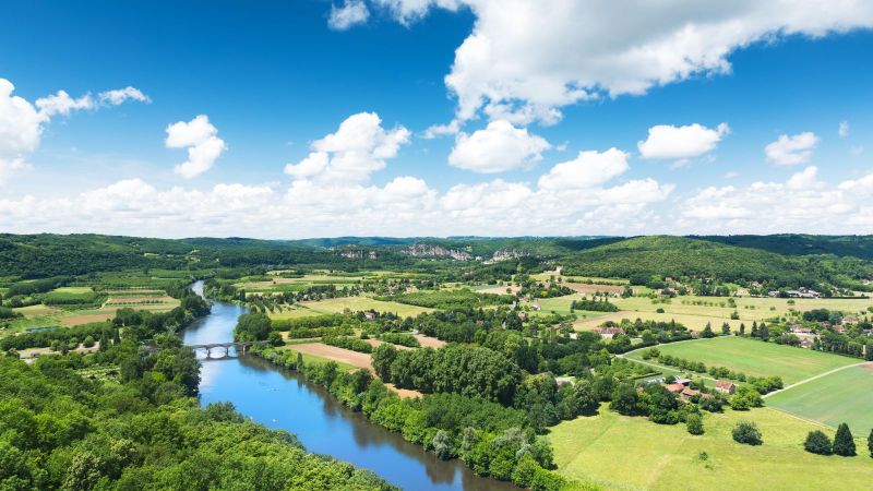 Panoramablick auf das Tal der Dordogne in Frankreich. Ein Fluss fließt durch eine Landschaft mit Feldern, Wäldern und kleineren Dörfern.
