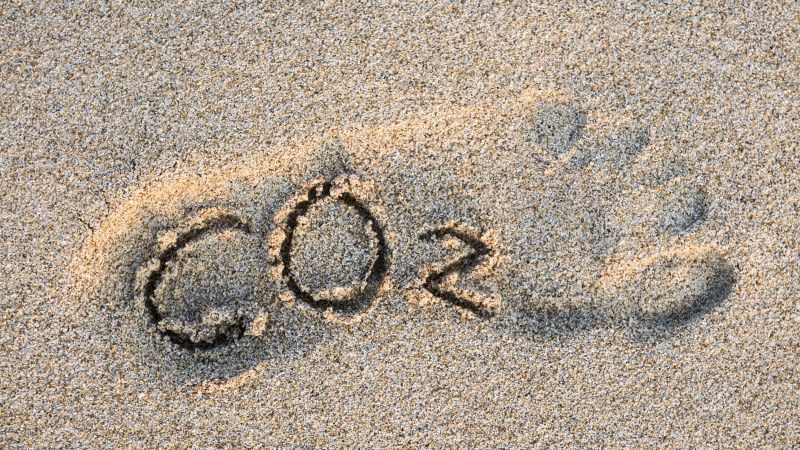 CO2-Text im Umriss eines Fußes in goldenem Sand.