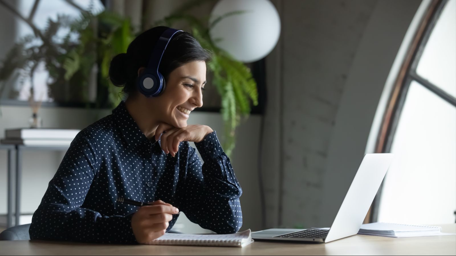 Eine Frau sitzt mit Kopfhörern an einem Schreibtisch vor einem Laptop.