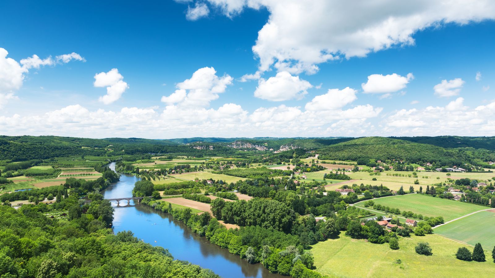 Panoramablick auf das Tal der Dordogne in Frankreich. Ein Fluss fließt durch eine Landschaft mit Feldern, Wäldern und kleineren Dörfern.